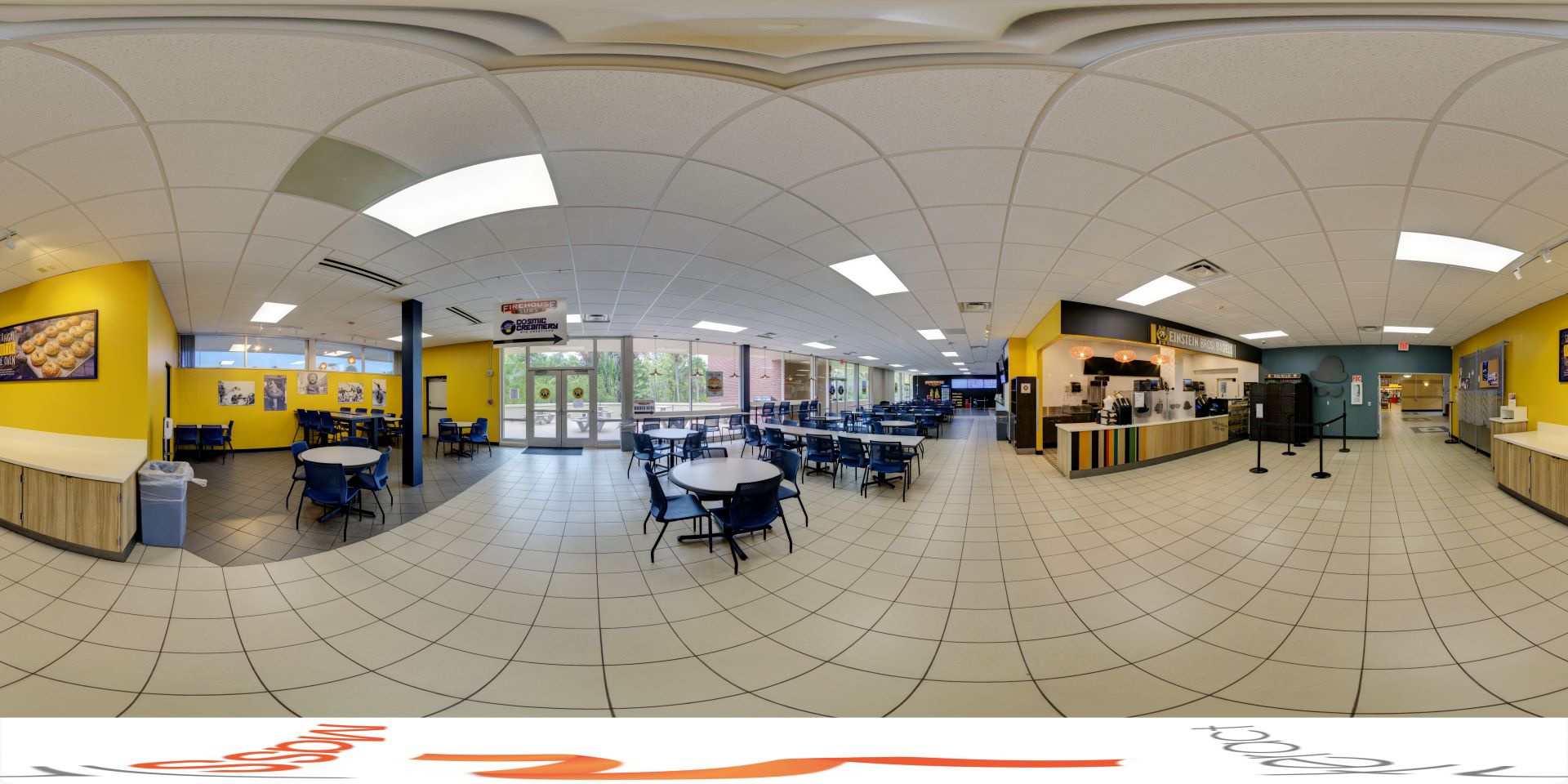 The panoramic image displays a spacious food court with a bright, inviting atmosphere. The area features yellow walls, round tables with blue chairs, and a clean, tiled floor